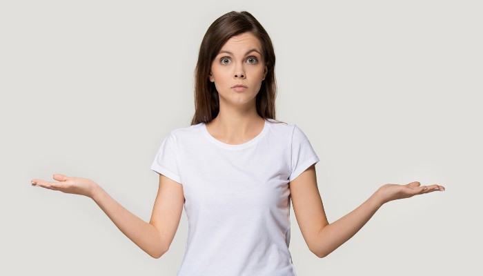 A young woman in a white T-shirt holding her arms in a questioning pose.